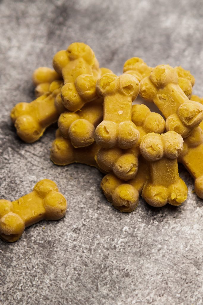 Stack of bone-shaped frozen pumpkin peanut butter dog treats on a gray surface.
